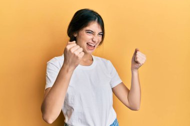 Beyaz gündelik tişört giyen genç beyaz kadın gururla bağırıyor zaferi ve başarıyı kutluyor. Kollarını kaldırarak heyecanlanıyor. 