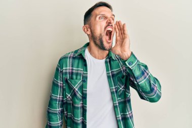 Sakallı, sıradan kıyafetler giyen, eli ağızda bağırıp çağıran yakışıklı bir adam. iletişim konsepti. 