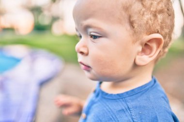 Sevimli ve mutlu küçük çocuk güneşli bir günde parkta eğleniyor. Güzel sarı saçlı erkek çocuk dışarıda oynuyor.
