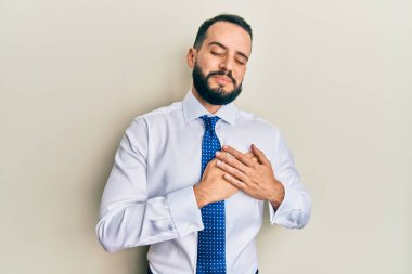 Sakallı, iş kravatı takan, elleri göğsünde, gözleri kapalı ve yüzünde minnet ifadesi olan genç bir adam. sağlık kavramı. 