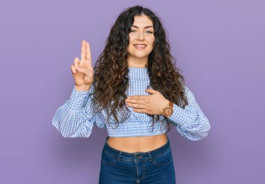 Gündelik kıyafetler giyen genç İspanyol kız gülümseyerek yemin ediyor, elleri göğsünde ve parmakları havada küfür ediyor, sadakat yemini ediyor. 