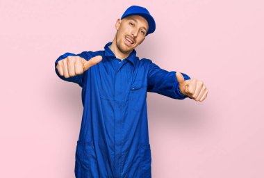 Sakallı, inşaatçı tulumu giymiş, kel bir adam elinle olumlu jest yapmayı onaylıyor, gülümsüyor ve başarı için seviniyor. kazanan jest. 