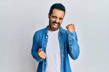 Gündelik giysiler giyen genç İspanyol adam şaşkınlık ve şaşkınlık içinde kollarını kaldırarak ve gözlerini kapayarak başarıyı kutluyor. 