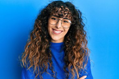 Sıradan kıyafetler ve gözlük takan, kollarını kavuşturup kameraya gülümseyen genç İspanyol kız. pozitif kişi. 