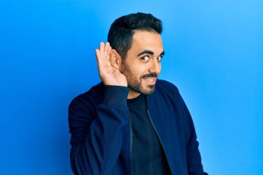 Gündelik kıyafetler giyen, ağzı kulaklarında gülümseyen, dedikoduları ve dedikoduları dinleyen genç İspanyol bir adam. Sağırlık kavramı. 