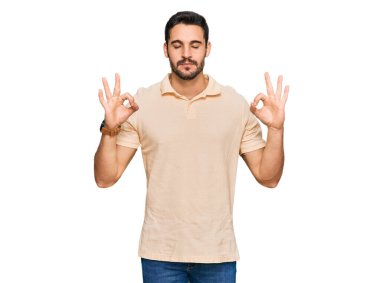 Günlük kıyafetler giyen genç İspanyol adam rahatla ve gözleri kapalı gülümse parmaklarıyla meditasyon hareketi yapıyor. yoga konsepti. 