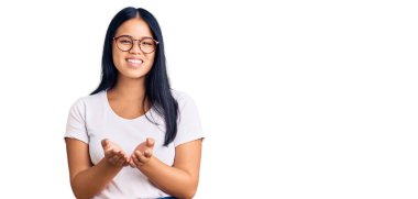 Elleri avuçlarında gülümseyen, günlük giysiler ve gözlük takan güzel Asyalı kız jest yapıyor ya da yapıyor. Bekleme ve koruma 