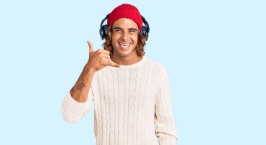 Genç İspanyol adam müzik dinliyor kulaklık takıyor gülümsüyor telefonla el ve parmaklarıyla jest yapıyor telefonda konuşuyor gibi. iletişim kavramları. 