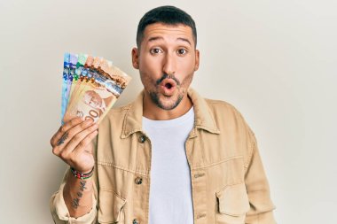 Kanada doları tutan yakışıklı bir adam ağzı açık kalmış, korkmuş ve şaşkına dönmüş, imansız bir yüz. 