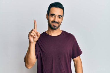 Bir fikir veya soruyla gülümseyen gündelik kıyafetler giyen genç İspanyol adam, bir numara, mutlu bir yüzle işaret ediyor. 