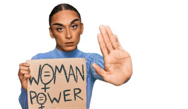 Makyajlı ve uzun saçlı İspanyol transseksüel adam. Değişiklik pankartı lazım. El açık, dur işareti yapıyor. 