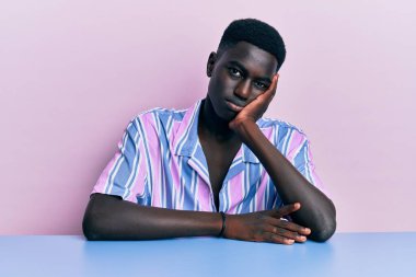 Genç, Afro-Amerikan bir adam, günlük giysiler içinde oturmuş kollarını kavuşturup depresyondan sıkılmış ve yorgun göründüğünü düşünüyor.. 
