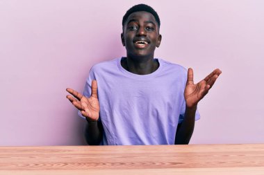 Gündelik giysiler giymiş genç Afrikalı Amerikalı adam zaferi mutlu bir gülümsemeyle ve ellerini kaldırarak kutluyor. 