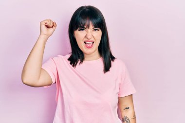 Genç İspanyol kadın rahat kıyafetler giyiyor kızgın ve kızgın yumruğunu kaldırıyor ve öfkeyle bağırıyor. öfke ve agresif konsept. 