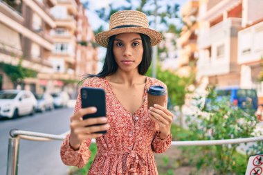 Akıllı telefon kullanan ve şehirde kahve içen ciddi yüzlü Afrikalı Amerikalı bir turist kadın..