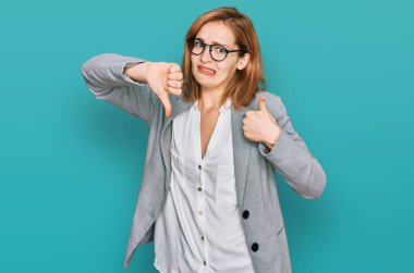İş tarzı giyinmiş, gözlüklü genç beyaz bir kadın baş parmak hareketi yapıyor. Anlaşmazlık ve uzlaşma ifadesi. çılgın çatışma 