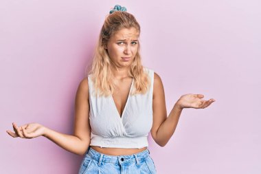 Sıradan kıyafetler giyen, elleri ve kolları havada, kafası karışmış genç sarışın kız. şüphe kavramı. 