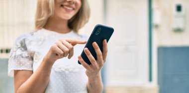 Beyaz kız şehrin caddesinde akıllı telefon kullanarak mutlu bir şekilde gülümsüyor..