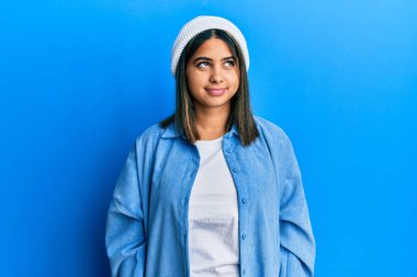 Tatlı yün şapkalı genç Latin kadın gülümsüyor, yan tarafa bakıyor ve düşünüyor.. 