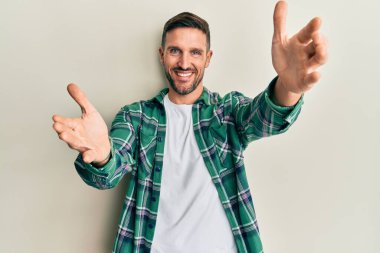 Sakallı, sıradan kıyafetler giyen yakışıklı kameraya sarılıp gülümseyen bir adam. Mutluluğu kucaklayan neşeli bir ifade.. 