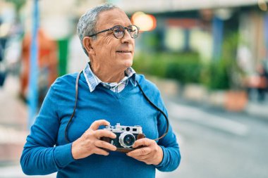 Yaşlı gri saçlı turist şehirde klasik kamera kullanarak mutlu bir şekilde gülümsüyor..