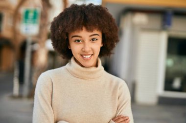 Kollarını kavuşturmuş genç İspanyol kız şehirde mutlu bir şekilde gülümsüyor..