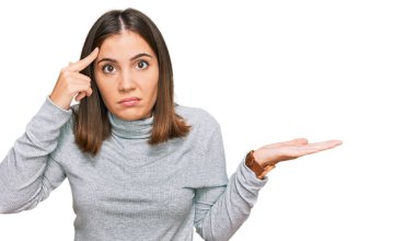 Balıkçı yaka kazak giyen genç ve güzel bir kadın avucunun içi açık, fotokopi alanı gösteren ve parmağıyla alnını gösteren bir kazak giyiyor. Bunu bir düşün.. 