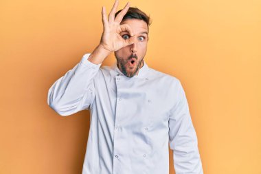 Profesyonel aşçı üniforması giyen sakallı yakışıklı adam şaşırmış yüz ifadesiyle şaşırmış, parmaklarından bakan gözler. İnançsız ifade. 