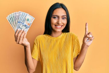 Elinde dolarlarla gülümseyen genç esmer kadın bir fikir veya soruyla mutlu bir yüzle işaret ediyor. 