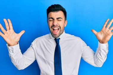 İş kıyafetleri giymiş genç İspanyol adam başarı için deli ve çılgınlığı kutluyor kollarını kaldırmış ve gözlerini kapatmış heyecanla bağırıyor. Kazanan konsept 