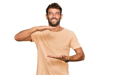 Sakallı, sıradan tişörtlü, elleri büyük ve büyük bir işaret gösteren yakışıklı bir genç. Ölçü sembolü. Kameraya bakıp gülümsüyor. ölçüm kavramı. 