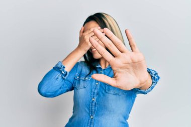 Sıradan kot ceket giyen genç İspanyol kadın elleriyle gözlerini kapatıyor ve üzgün ve korku ifadeleriyle dur hareketi yapıyor. utangaç ve olumsuz kavram. 