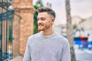 Genç beyaz adam gülümseyerek şehirde mutlu mesut duruyor..