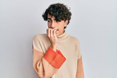 Kış süveteri giyen İspanyol genç adam gergin ve gergin görünüyor. Elleri ağızdan tırnak yiyor. anksiyete. 