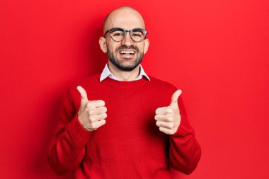 Genç kel bir adam günlük kıyafetler ve gözlük takıyor. Başarı işareti yapıyor. Elleriyle olumlu bir jest yapıyor. Neşeli ifade ve kazanan jest. 