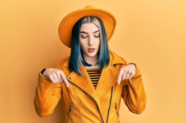 Sarı şapkalı, deri ceketli, reklamını gösteren, şaşırmış ve ağzı açık genç bir kız. 