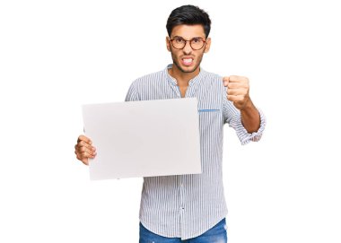 Boş pankart tutan yakışıklı genç adam sinirlenmiş ve sinirlenmiş öfkeyle bağırıyor, öfkeyle bağırıyor ve el kaldırıyor. 