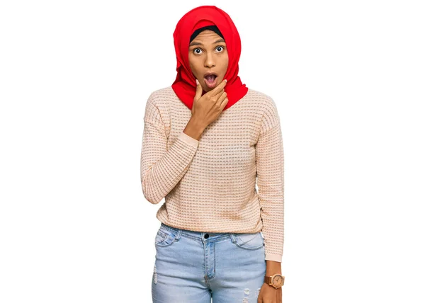 伝統的なイスラムのヒジャーブスカーフを身に着けている若いアフリカ系アメリカ人女性は 顎に手で不信感 驚きと驚きの表現に魅了されています — ストック写真