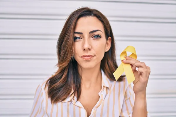 Young hispanic woman with serious expression holding awareness yellow ribon standing at the city.