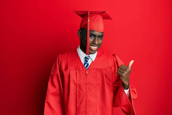 年轻的非洲裔美国人头戴毕业帽 身穿礼袍 面带微笑 面带微笑 并带着大拇指指向旁边 — 图库照片