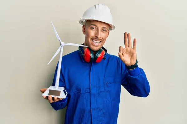 秃头的工程师 留着胡子 拿着太阳能风车进行可再生能源发电 手拿着手签 微笑着表示友善的手势 是极好的象征 — 图库照片