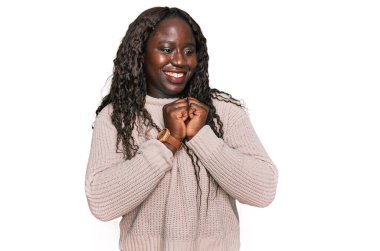 Kışın yün kazak giyen genç Afrikalı bir kadın gergin ve heyecanlı bir şekilde çenesinin kenarına bakıyor. 