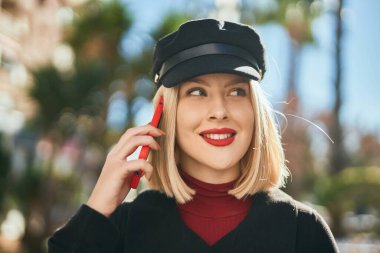 Genç sarışın kadın gülümsüyor. Şehirdeki akıllı telefondan konuşuyor..