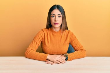 Masada oturan, gündelik kıyafetler giyen genç İspanyol kadın yüzünde ciddi bir ifadeyle rahatladı. Basit ve doğal bir şekilde kameraya bakıyorsun.. 