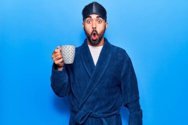 Uyku maskesi takmış, sabahlık giymiş, korkmuş ve ağzı açık bir şekilde şaşırmış genç İspanyol bir adam. 