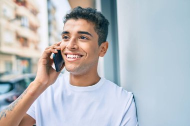 Genç Latin adam gülümsüyor. Şehirdeki akıllı telefondan konuşuyor..