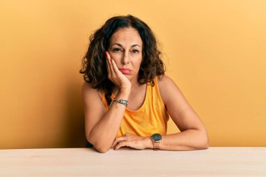 Masada oturan orta yaşlı güzel bir kadın kollarını kavuşturup depresyondan sıkılmış ve yorgun görünüyor.. 