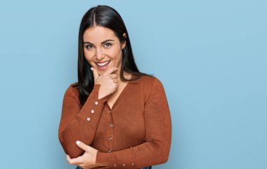 Gündelik kıyafetler giyen genç İspanyol kadın kameraya kendinden emin bakıyor kollarını kavuşturup gülümsüyor ve çenesini kaldırıyor. Olumlu düşünmek. 