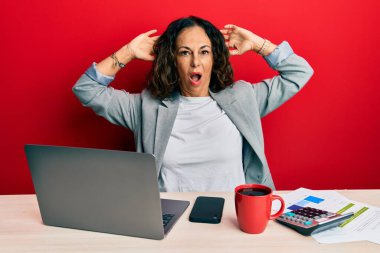 Ofiste çalışan orta yaşlı güzel bir kadın deli gibi bir fincan kahve içiyor ve elleri başının üstünde korkmuş ve ağzı açık bir şekilde şok geçirmekten korkuyor. 