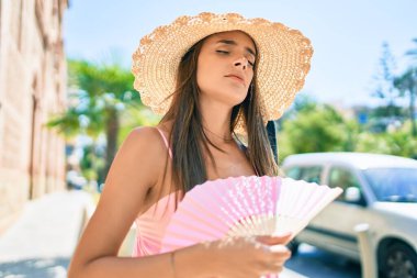 Tatilde olan genç İspanyol kadın yaz stili giyiniyor. Şehrin sokaklarında el yelpazesi kullanıyor.